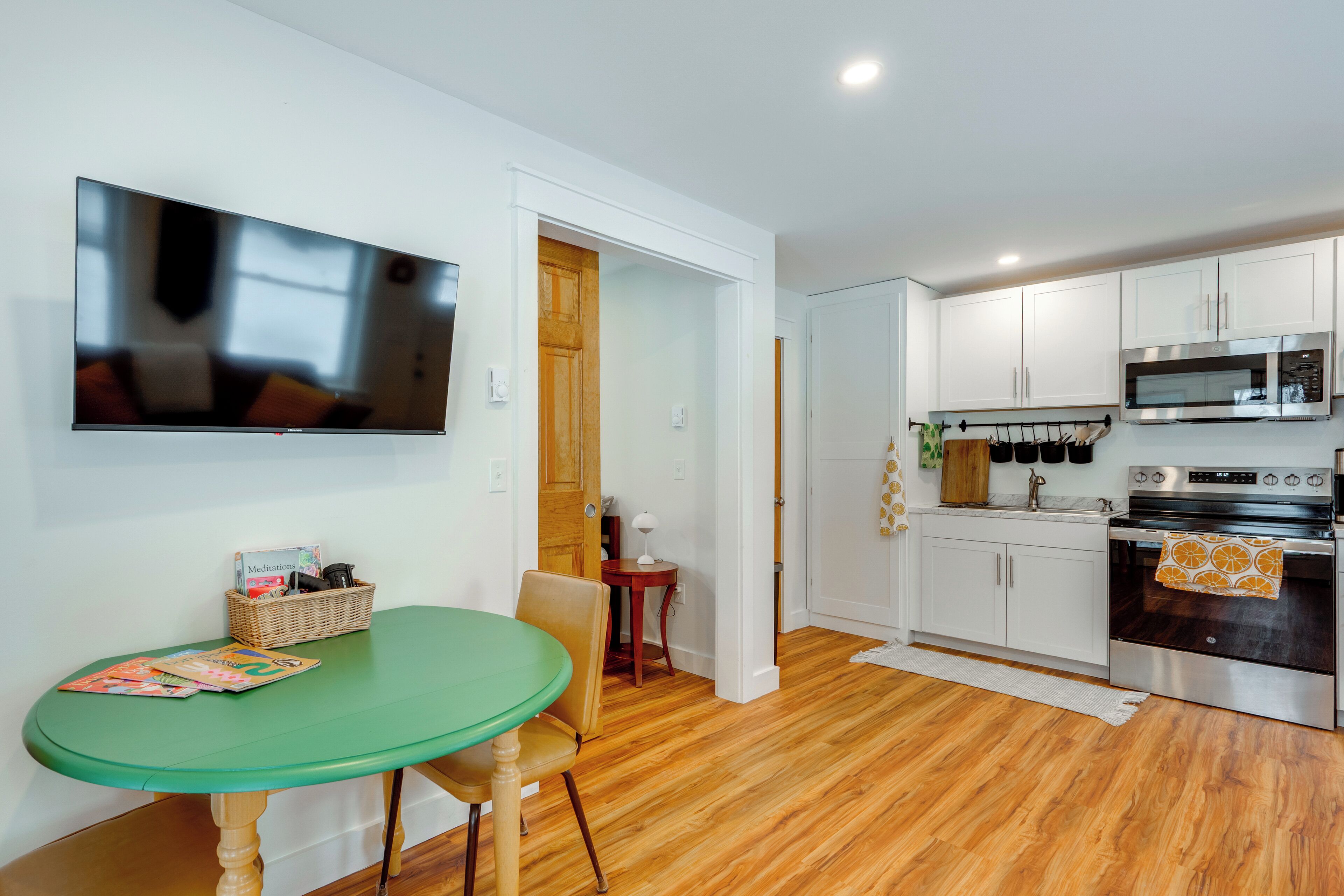 A compact kitchen with white cabinets, a microwave, and an oven. There's a dining area with a green table and chairs.
