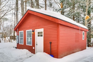 Eine rote Holzhütte mit weißer Tür und Fenstern, umgeben von Schnee und Bäumen.