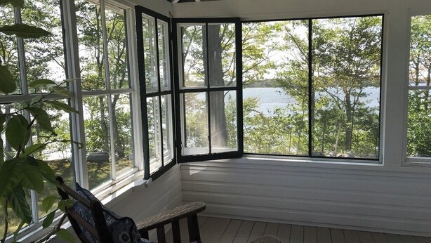Eine überdachte Veranda mit Blick auf einen See und Bäume.