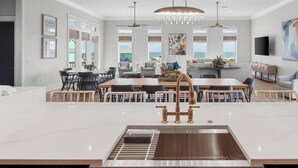 Une cuisine spacieuse dotée d’un îlot central, d’un évier en acier inoxydable et de luminaires suspendus.
