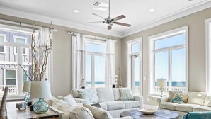 Un ampio soggiorno con ampie finestre, una ventola a soffitto e vista sull'oceano.