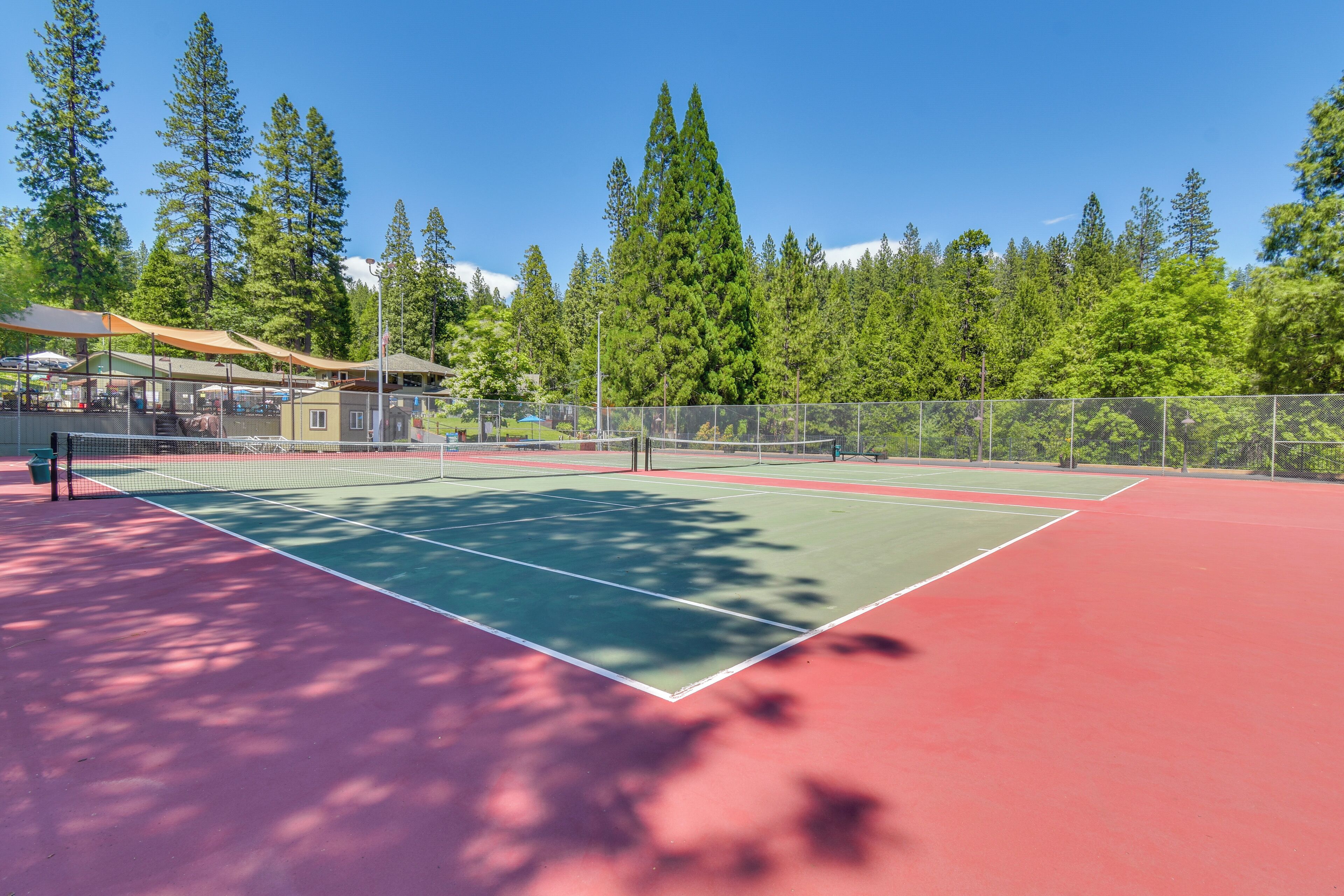 Un court de tennis avec un filet, entouré d’une clôture et d’arbres.