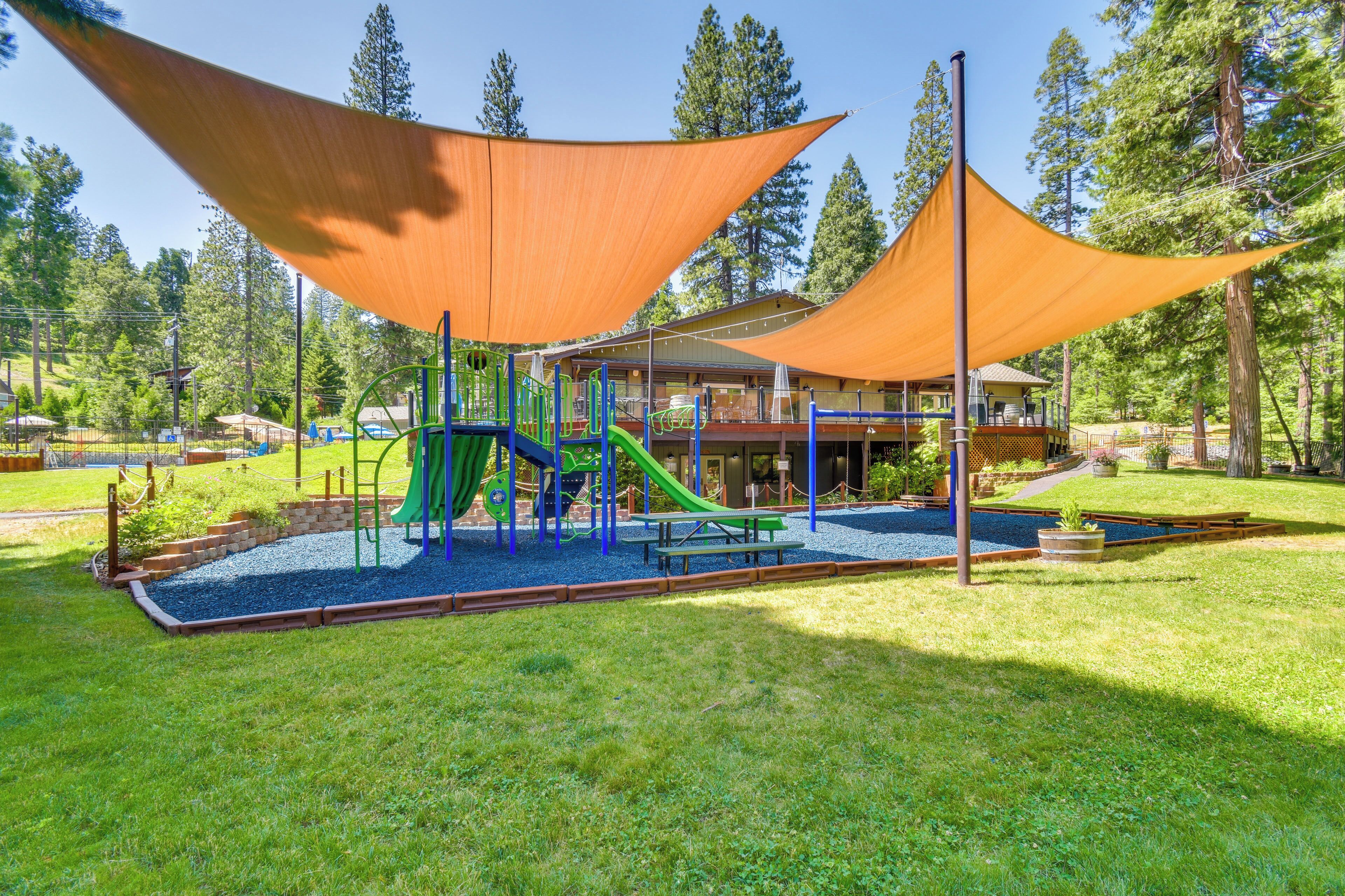 Ein Spielplatz mit Rutschen und einem Picknicktisch, umgeben von Gras und Bäumen.