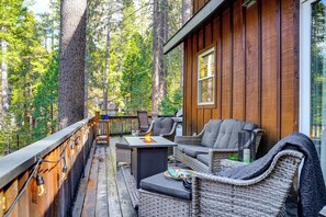A wooden deck with wicker furniture, a fire pit, and a view of a forest. - Game Room & Hot Tub! Dog-friendly Arnold Retreat (Arnold)