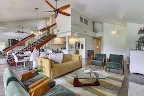 A spacious living area with a high ceiling, a staircase, and a kitchen in the background. - Palm Desert Gem w/ Outdoor Oasis & Resort Perks! (Palm Desert)