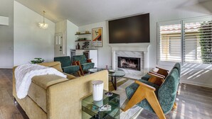 Ein Wohnzimmer mit einer Couch, Sesseln, einem Glastisch, einem Kamin und einem Fernseher.