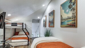 Ein kleines Hotelzimmer mit Etagenbetten, einem Glastisch und einem Bild einer tropischen Landschaft.