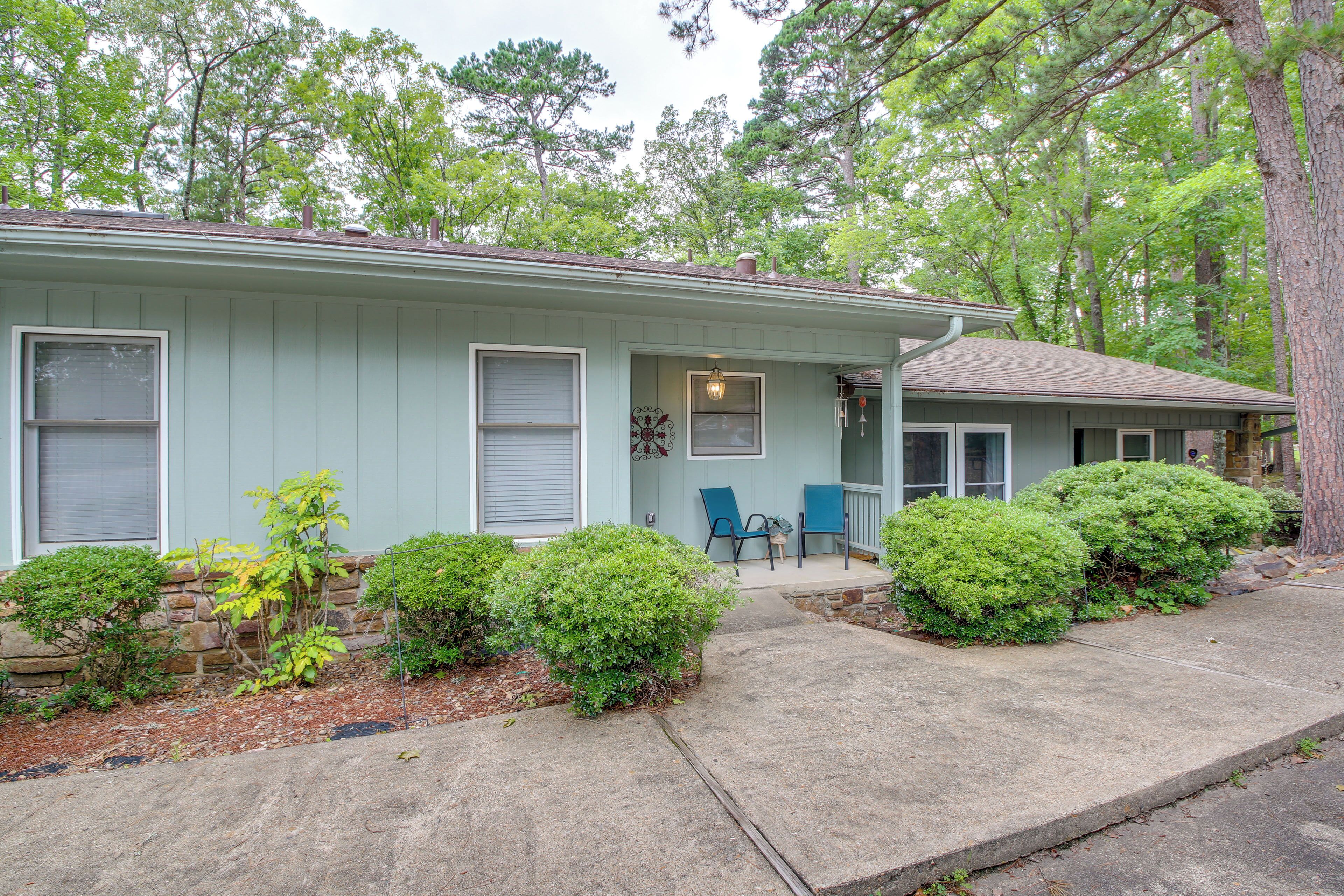 A light blue single-story house with a front porch, a small garden with bushes, and a stone wall.