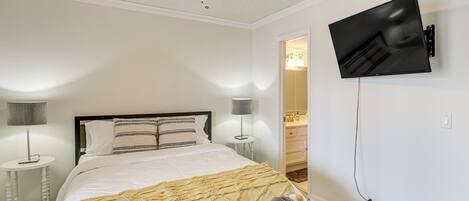 Une chambre à coucher comprenant un lit, un ventilateur de plafond, un téléviseur fixé au mur et une petite table de chevet avec une lampe.