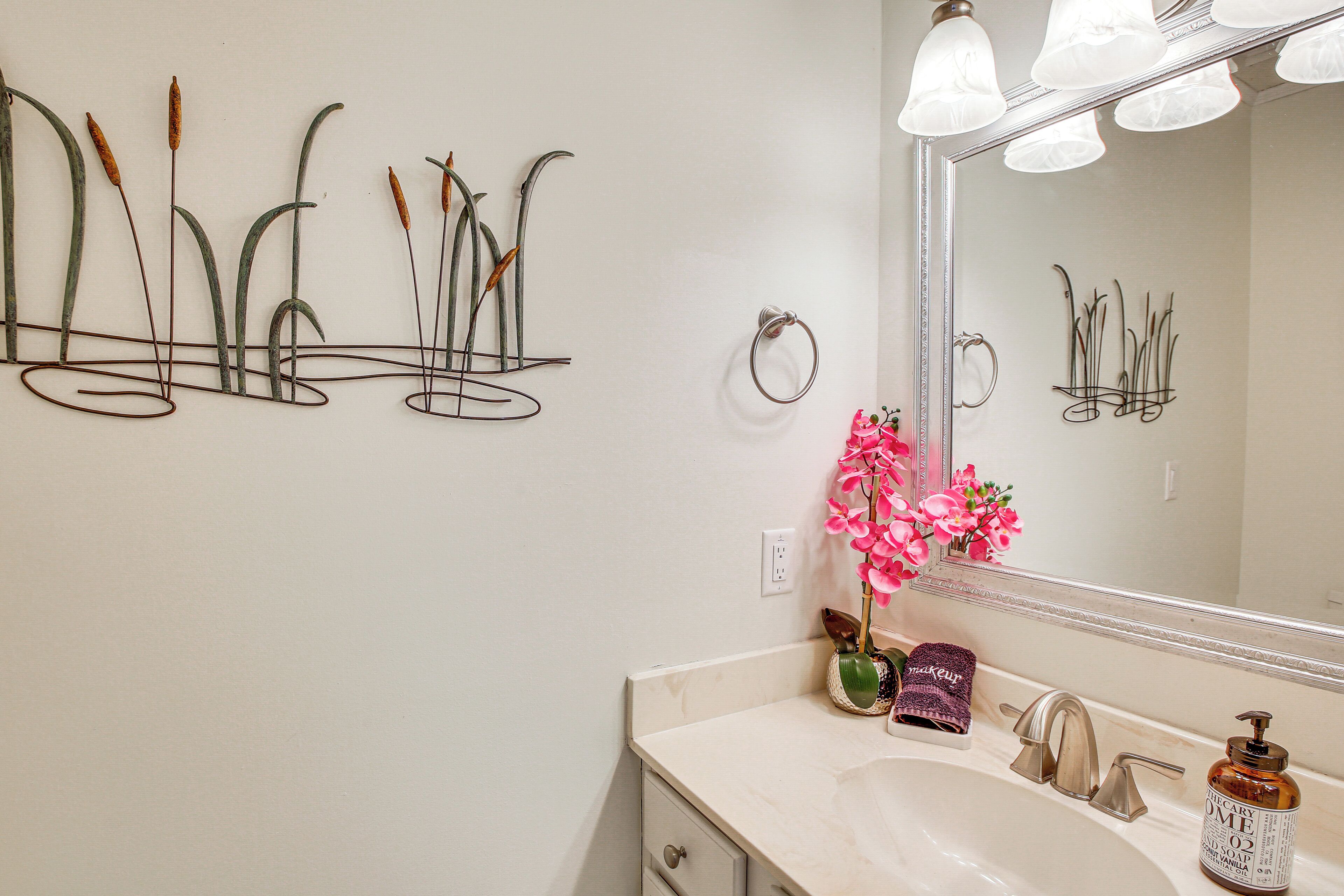 A bathroom with a white sink, a mirror, and a wall-mounted metal plant decoration.