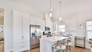A modern kitchen with white cabinetry, stainless steel appliances, and a central island with bar stools. - Blessing By The Bay | Community Pool | Sleeps 8 (Galveston)
