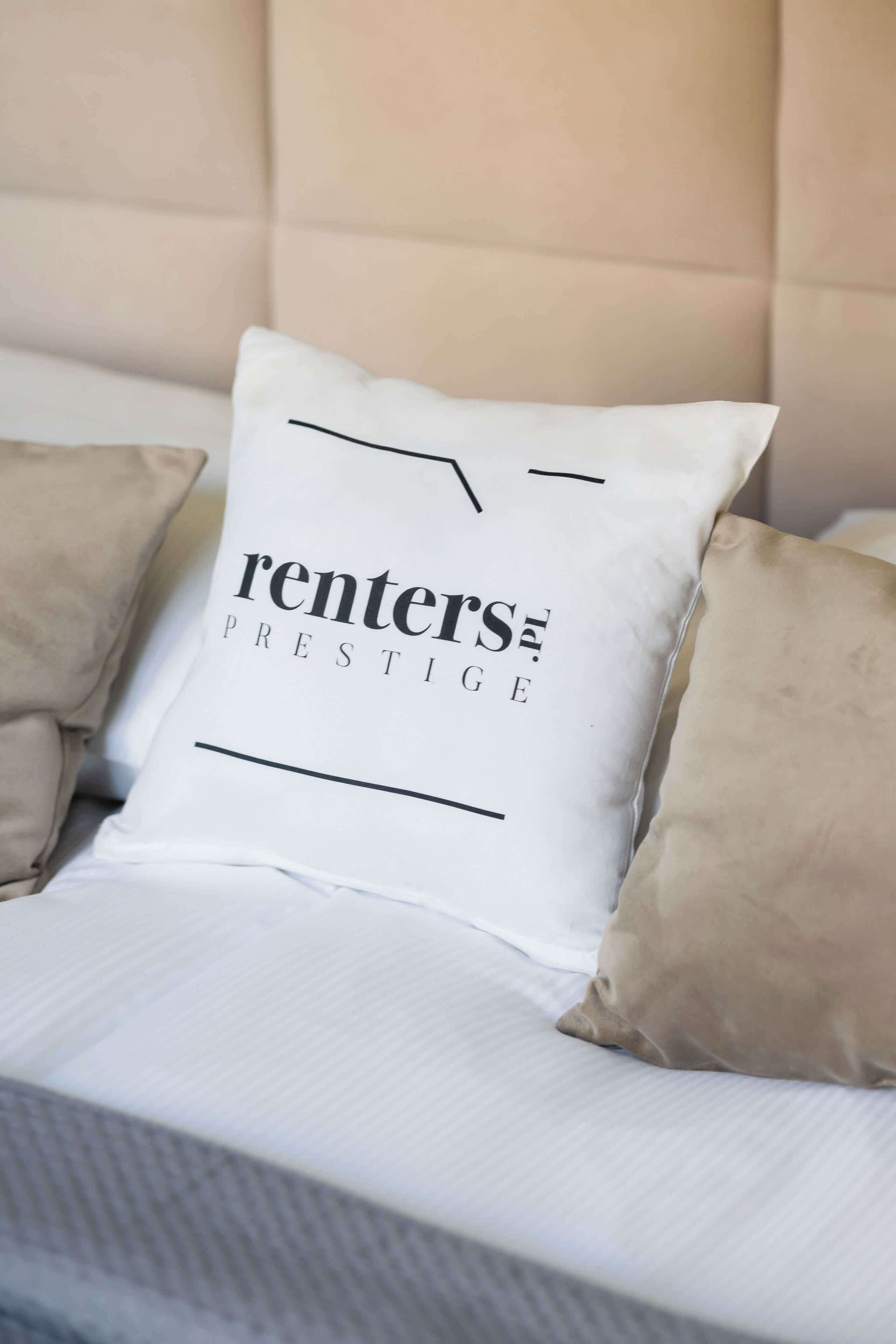 A bed with a white pillow featuring the text "renter's prestige" and a beige pillow.