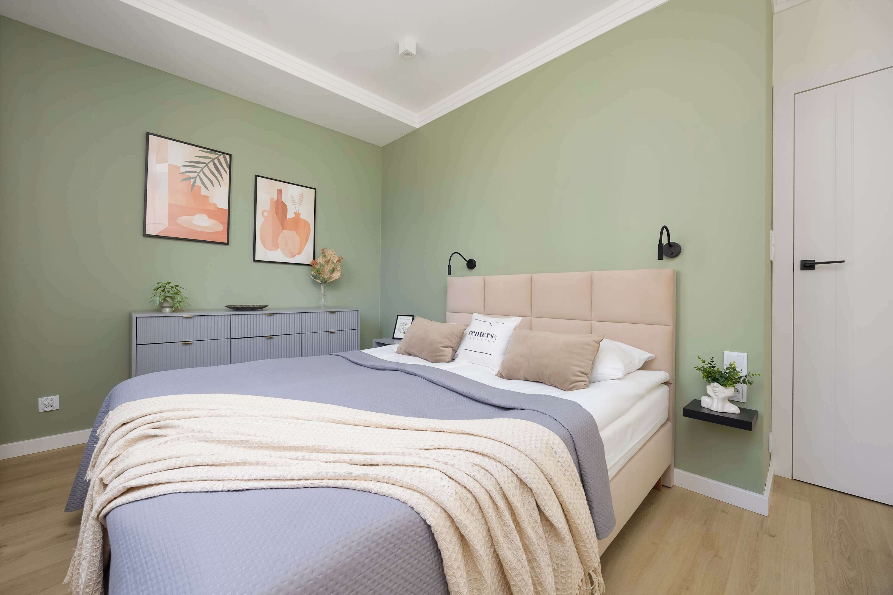 Quarto com cama, mesa de cabeceira, cômoda e duas luminárias fixadas na parede.