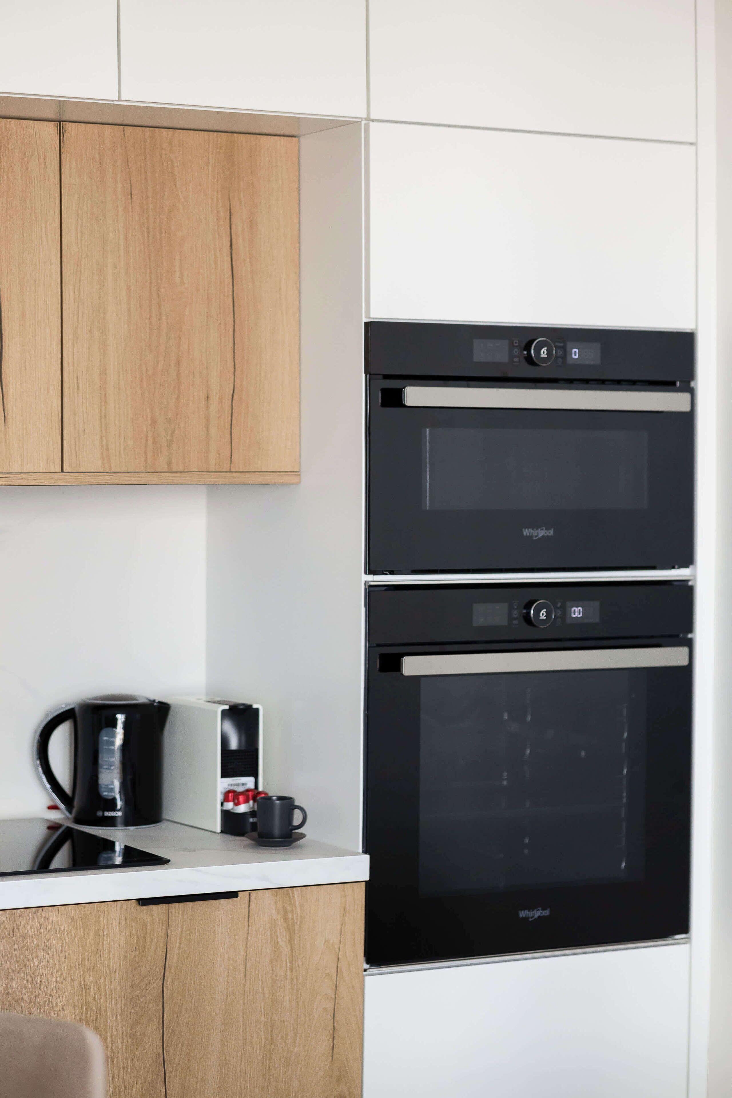 A modern kitchen with two Whirlpool ovens, a coffee maker, and a cup on the counter.