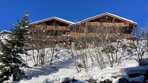 Un chalet en bois doté d’un balcon, entouré d’arbres couverts de neige et surplombant un ciel bleu clair.