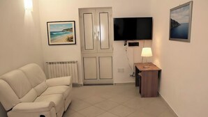 Una habitación con un sofá blanco, televisión, lámpara y un cuadro en la pared.
