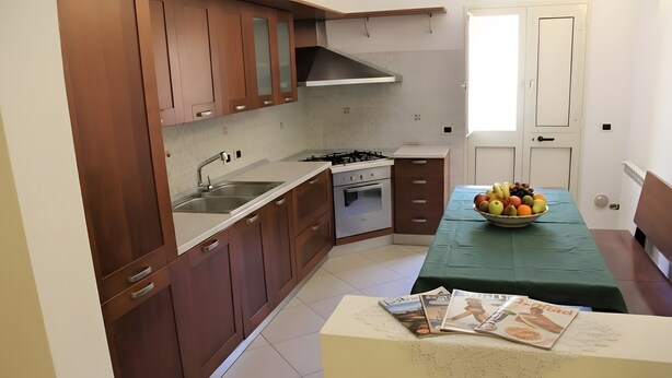 Una cocina con armarios de madera, una estufa a gas, un lavamanos y una mesa de comedor con un bol de fruta.