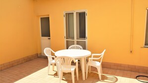 Un patio con una mesa y sillas blancas, una puerta corredera de vidrio y una ventana.