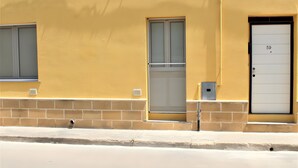 Un edificio con fachada amarilla, una puerta numerada 59 y un ventanal con persiana.