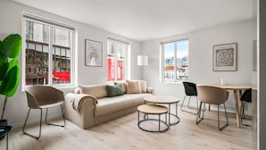 A modern living room with a sofa, two chairs, a small table, and large windows offering city views. - City Center, Light & Modern Apartment (Bergen)
