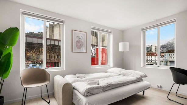A modern bedroom with a bed, two chairs, a large window, and a plant. - City Center, Light & Modern Apartment (Bergen)