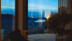 Vista da una stanza con ampie finestre che si affacciano su una città al crepuscolo.