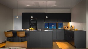 Una cucina moderna con isola centrale, mobili scuri e luci a sospensione.