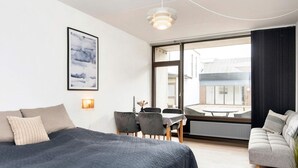 Ein modernes Schlafzimmer mit einem großen Bett, einem Essbereich mit Stühlen, einer Couch und Blick ins Freie.