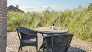 Ein runder Tisch mit zwei Korbstühlen, einer Backsteinmauer und hohem Gras im Hintergrund.