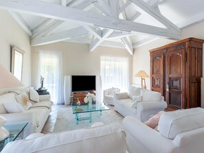 Un salon spacieux, meublé de meubles blancs, avec une table basse en verre et un grand meuble en bois.