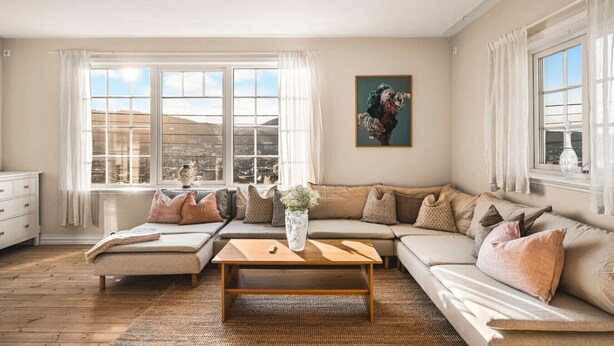 A living room with a large sectional sofa, a wooden coffee table, and a view of a cityscape through large windows. - Charming Home with Spectacular Views - NEW! (Bergen)