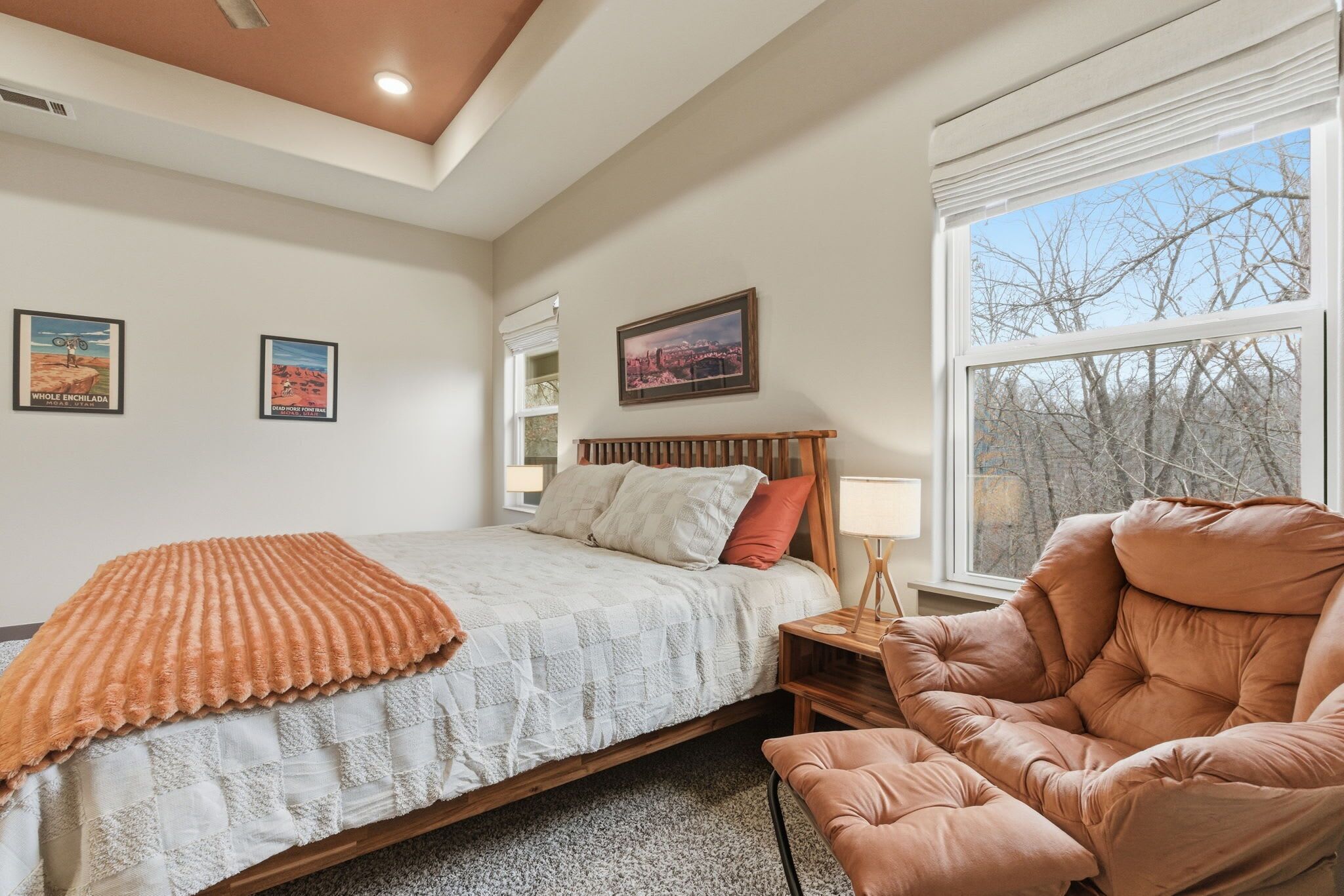 A bedroom with a bed, a chair, a nightstand, and a window with a view of trees.