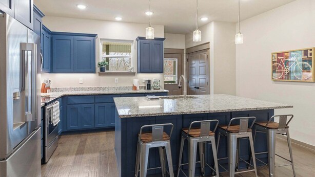 A modern kitchen with blue cabinets, a granite countertop, stainless steel appliances, and bar stools. - The Allendale Overlook (Bella Vista)