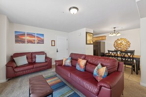 A living room with a red leather sofa, a striped rug, and a dining area with a wooden table and chairs. - New Listing! Adventure Ready | Near Arches | Hot Tub + Pool | Views (Moab)