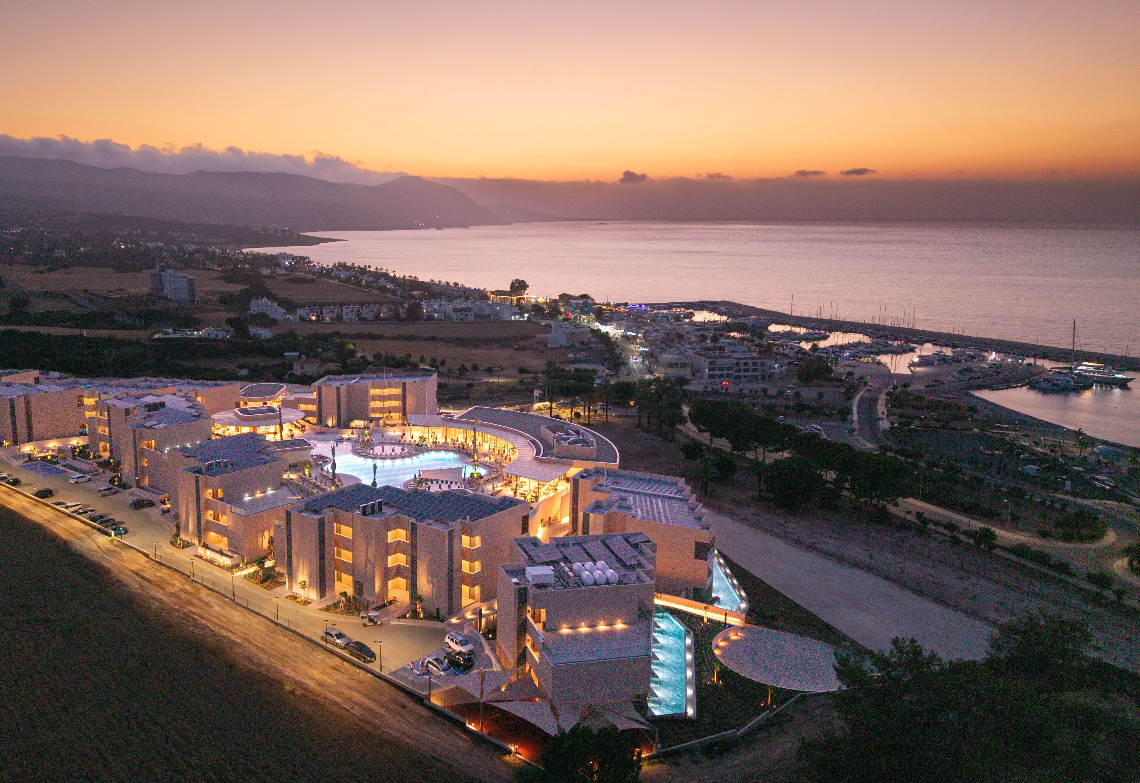 A hotel with a swimming pool, multiple buildings, and a view of the sea.