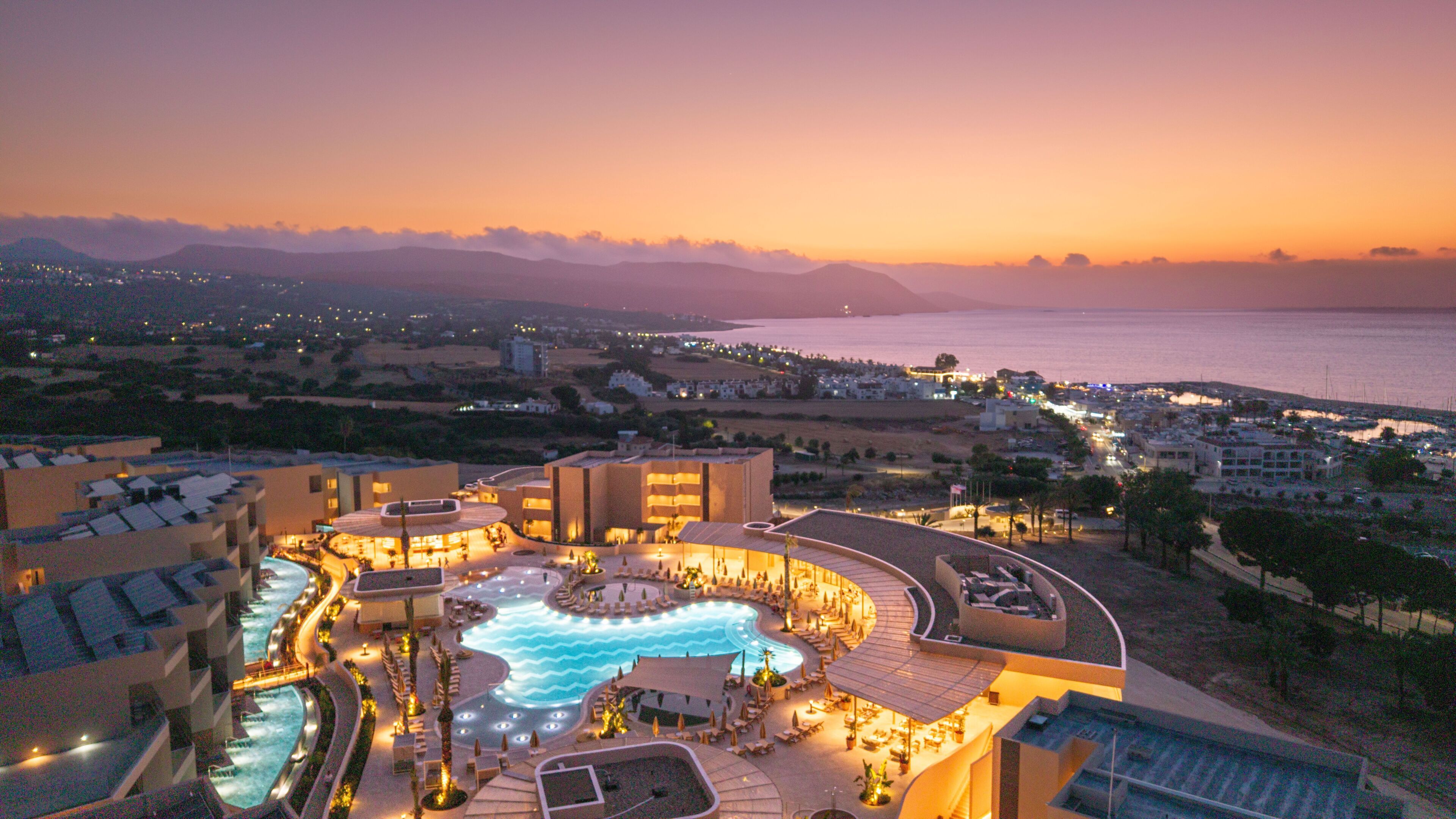 Ein Resort mit Pool, mehreren Gebäuden und Blick auf das Meer im Abenddämmerung.
