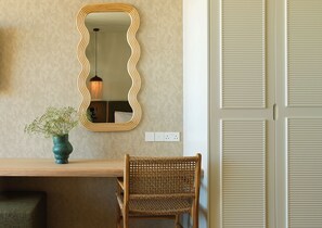 A room with a wooden desk, a wicker chair, a mirror, and a hanging light fixture. - NALU Latchi Leonardo Limited Edition (Polis)