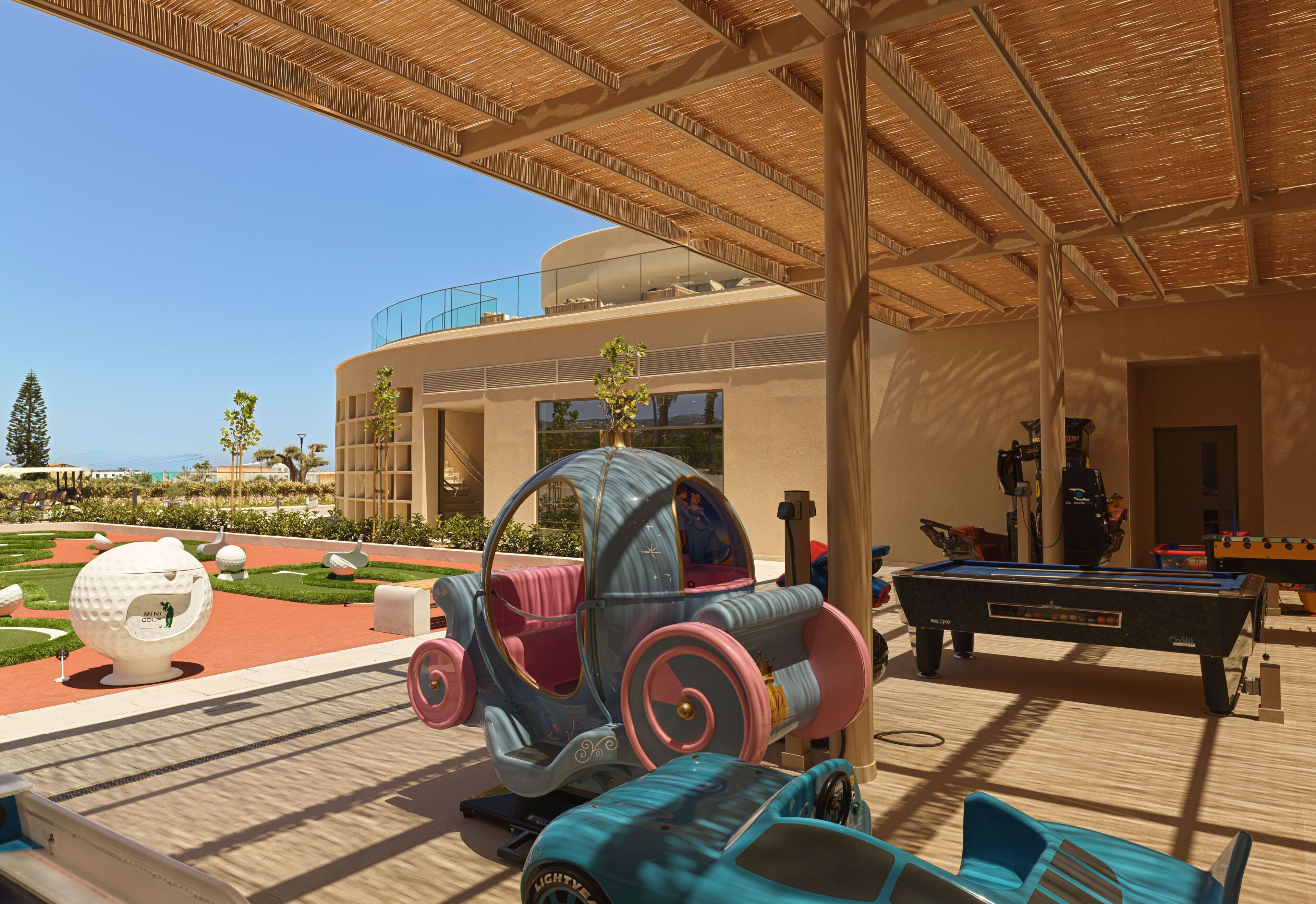 A modern outdoor area with a pool table, a children's ride-on toy, and a golf ball sculpture.