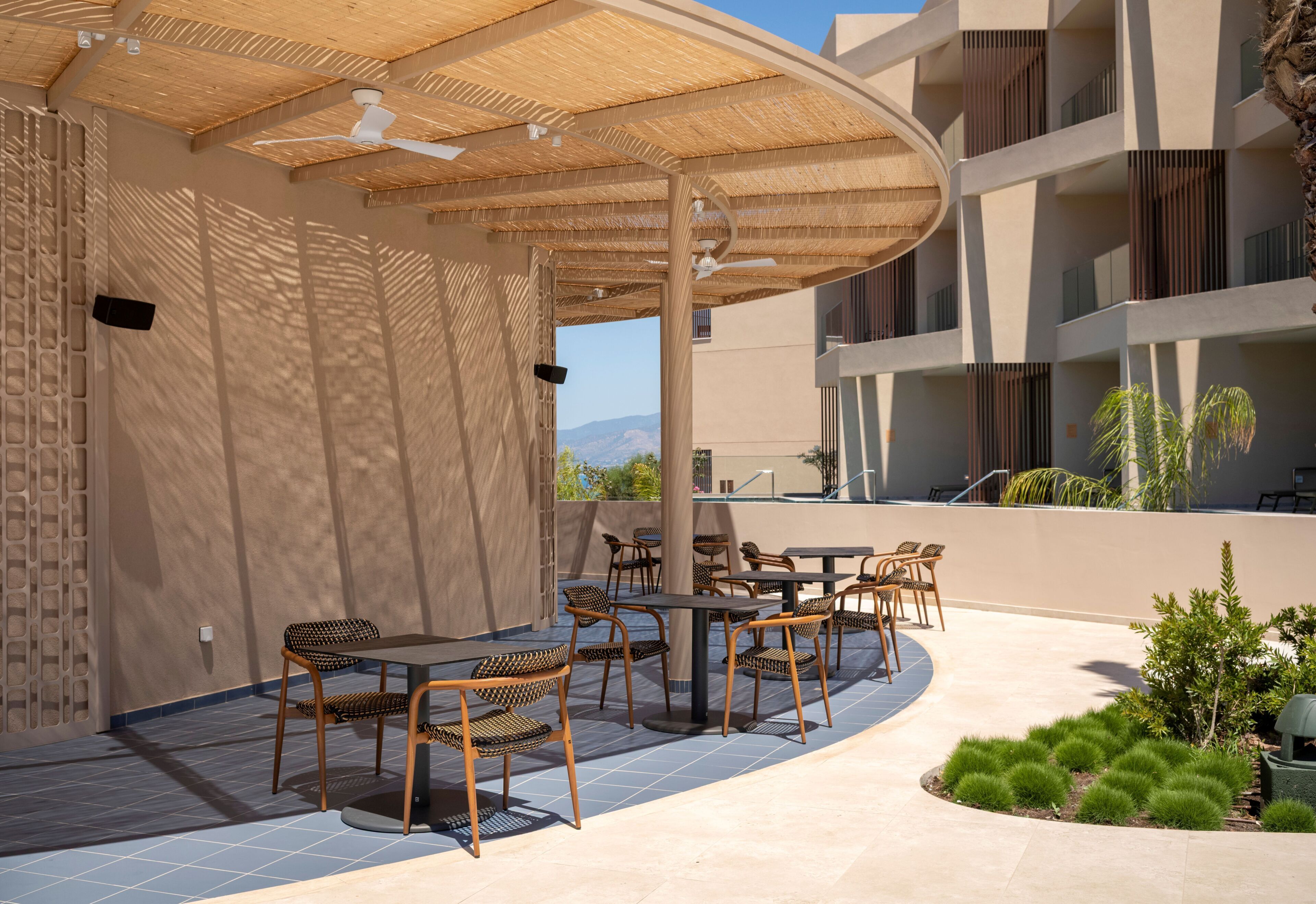 Un espacio exterior con mesas y sillas, una zona cubierta con ventilador de techo y vistas del paisaje circundante.