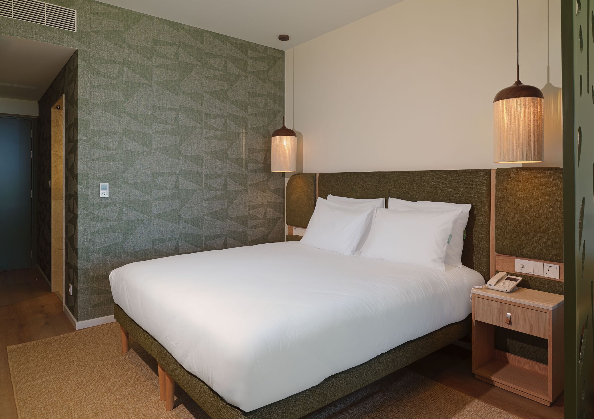 Een hotelkamer met een bed, nachtkastje, lamp en een behang met patroon.