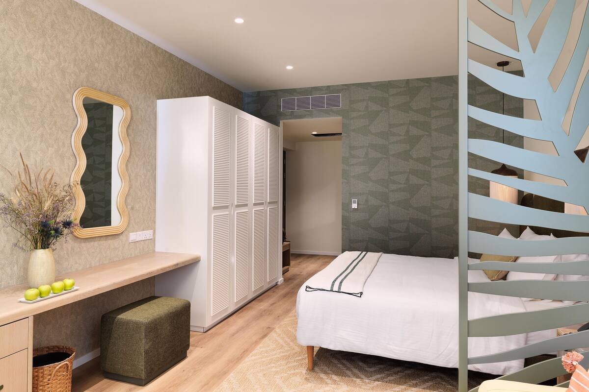 Un dormitorio con cama, armario, tocador con espejo y una pequeña banca.