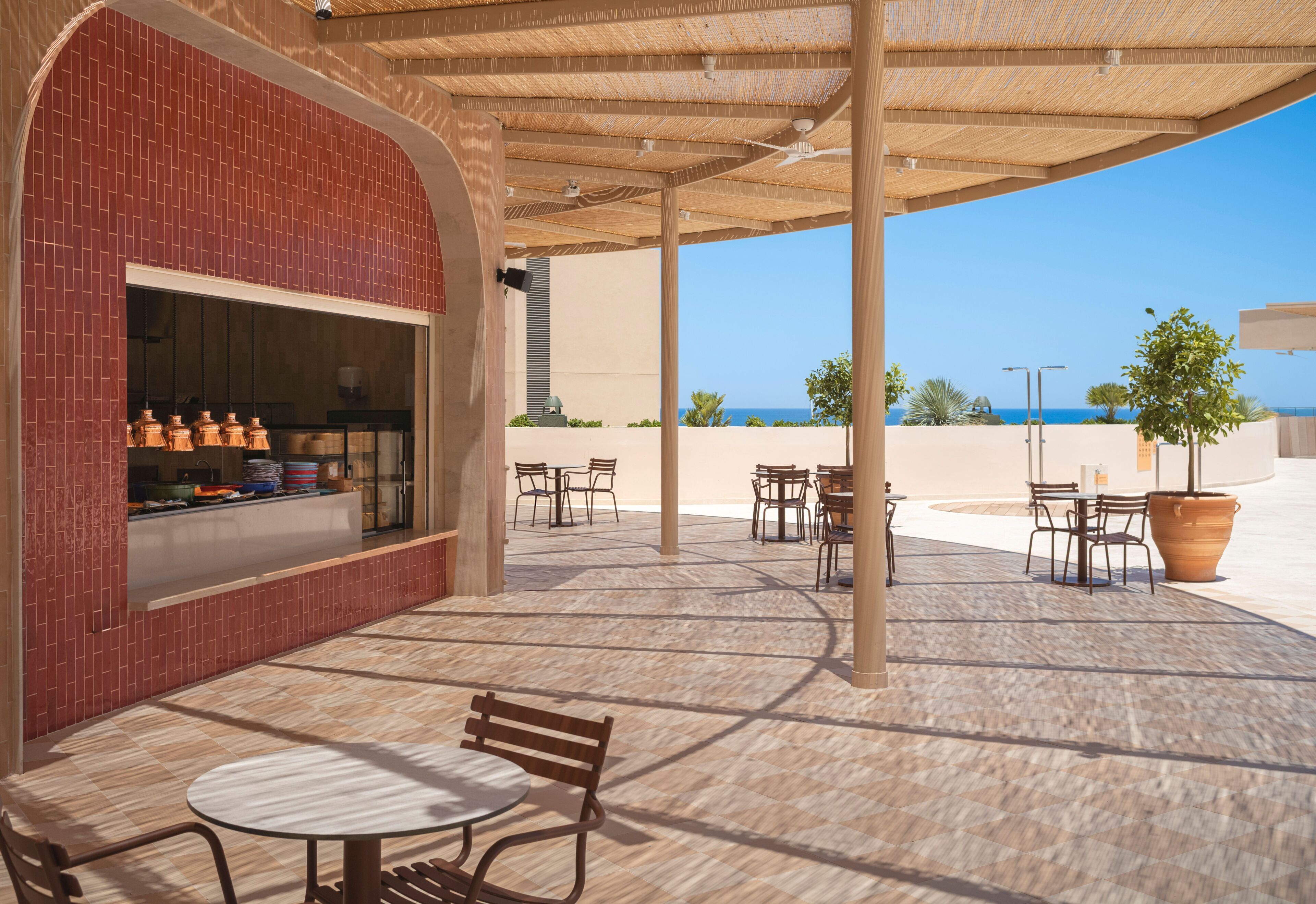 Un espace extérieur aménagé en terrasse, avec des tables et des chaises, un mur en briques et une vue sur la mer.