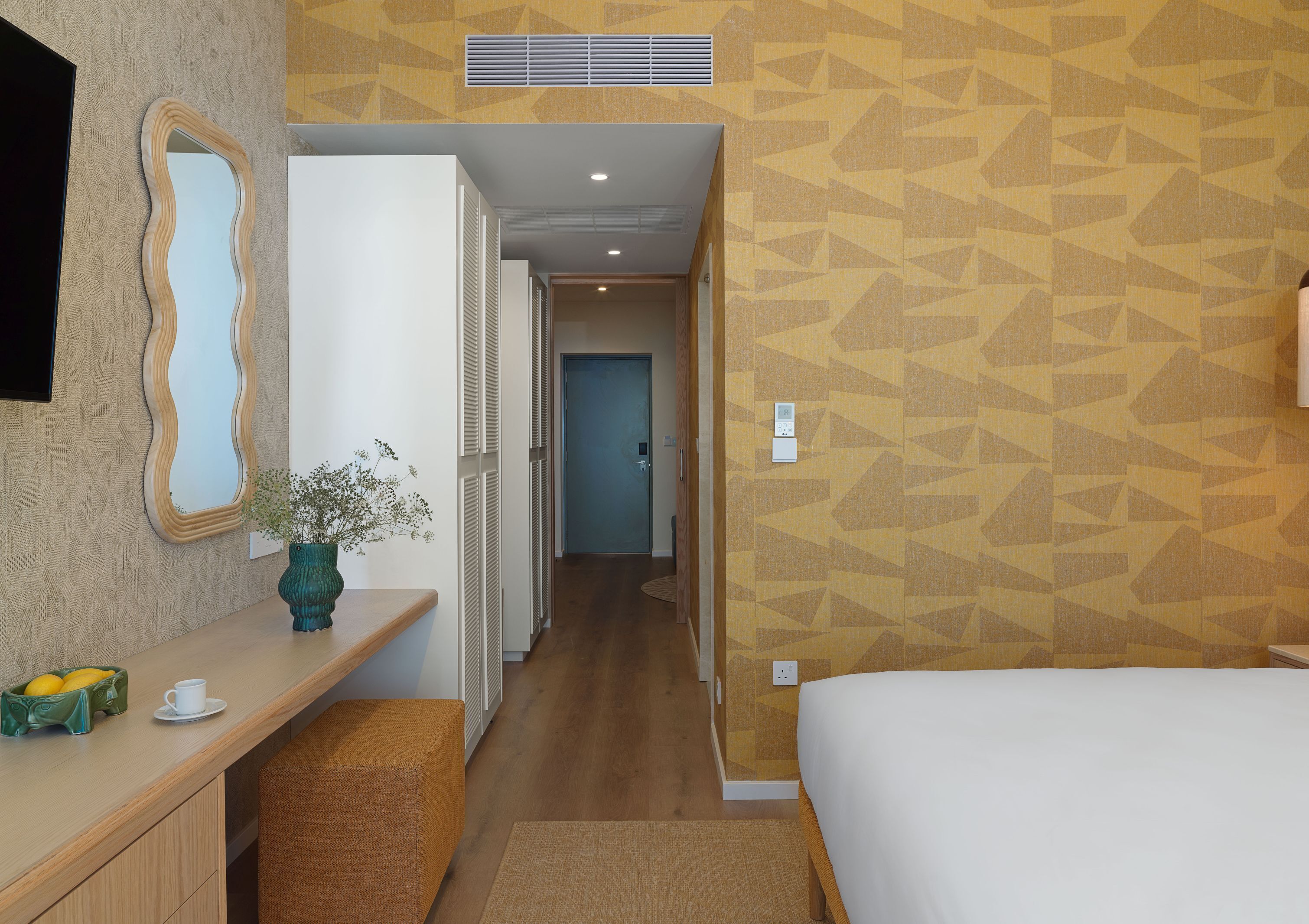 Habitación de hotel con cama, escritorio con un florero, espejo y pared con diseño.