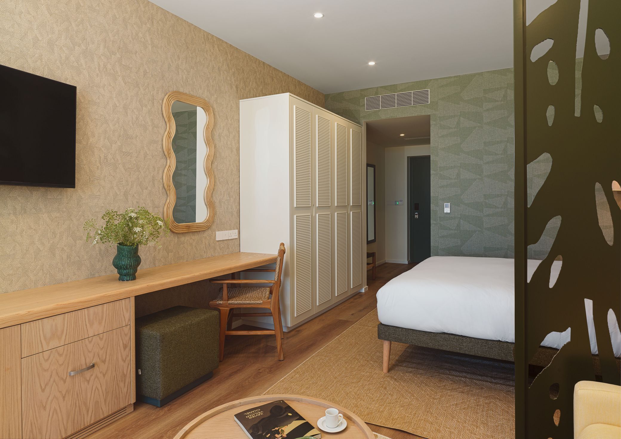 Quarto de hotel com escrivaninha de madeira, uma cadeira, uma cama, televisão e guarda-roupa.