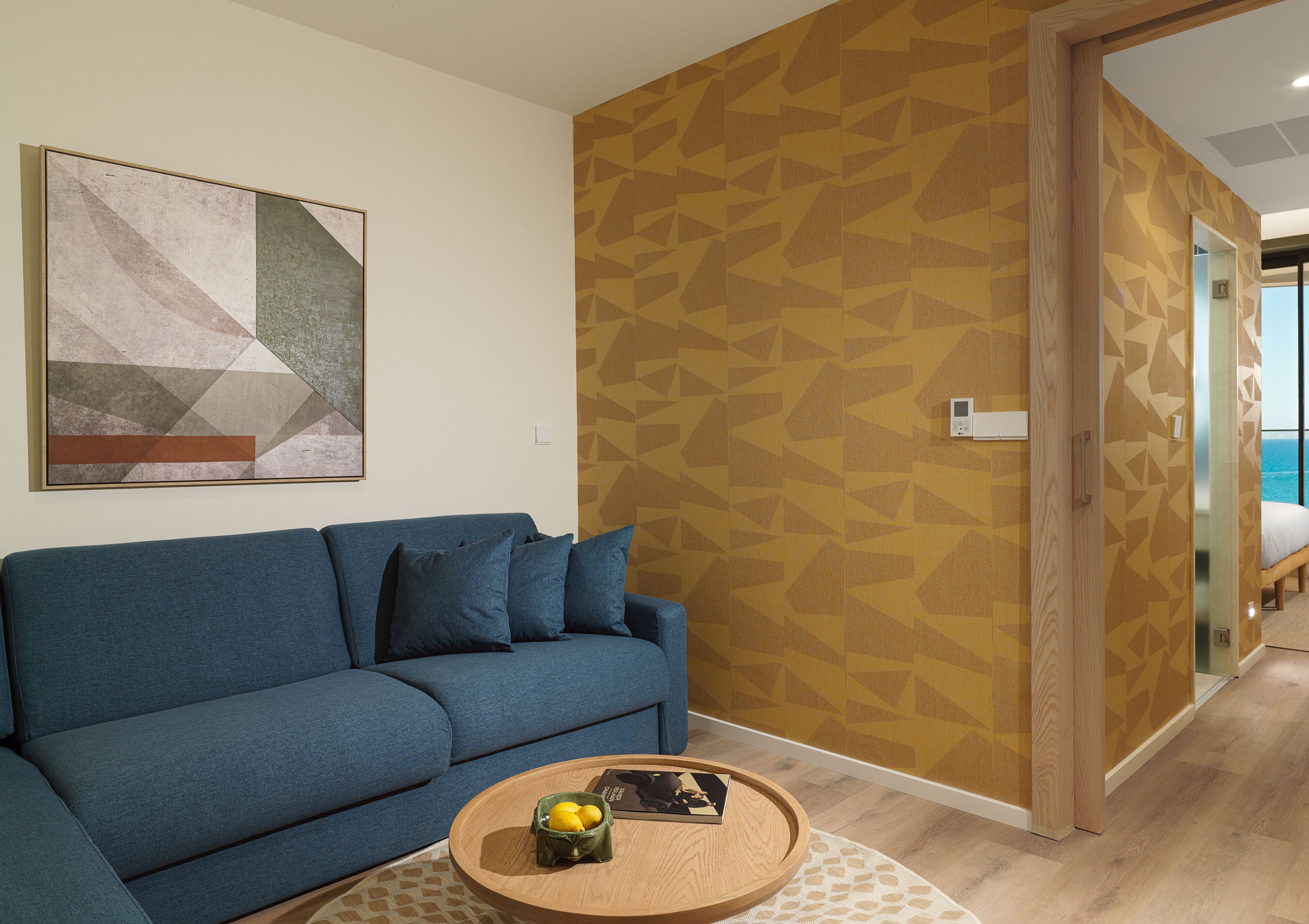 A living room with a blue sofa, a coffee table with a fruit bowl, and a patterned wall.