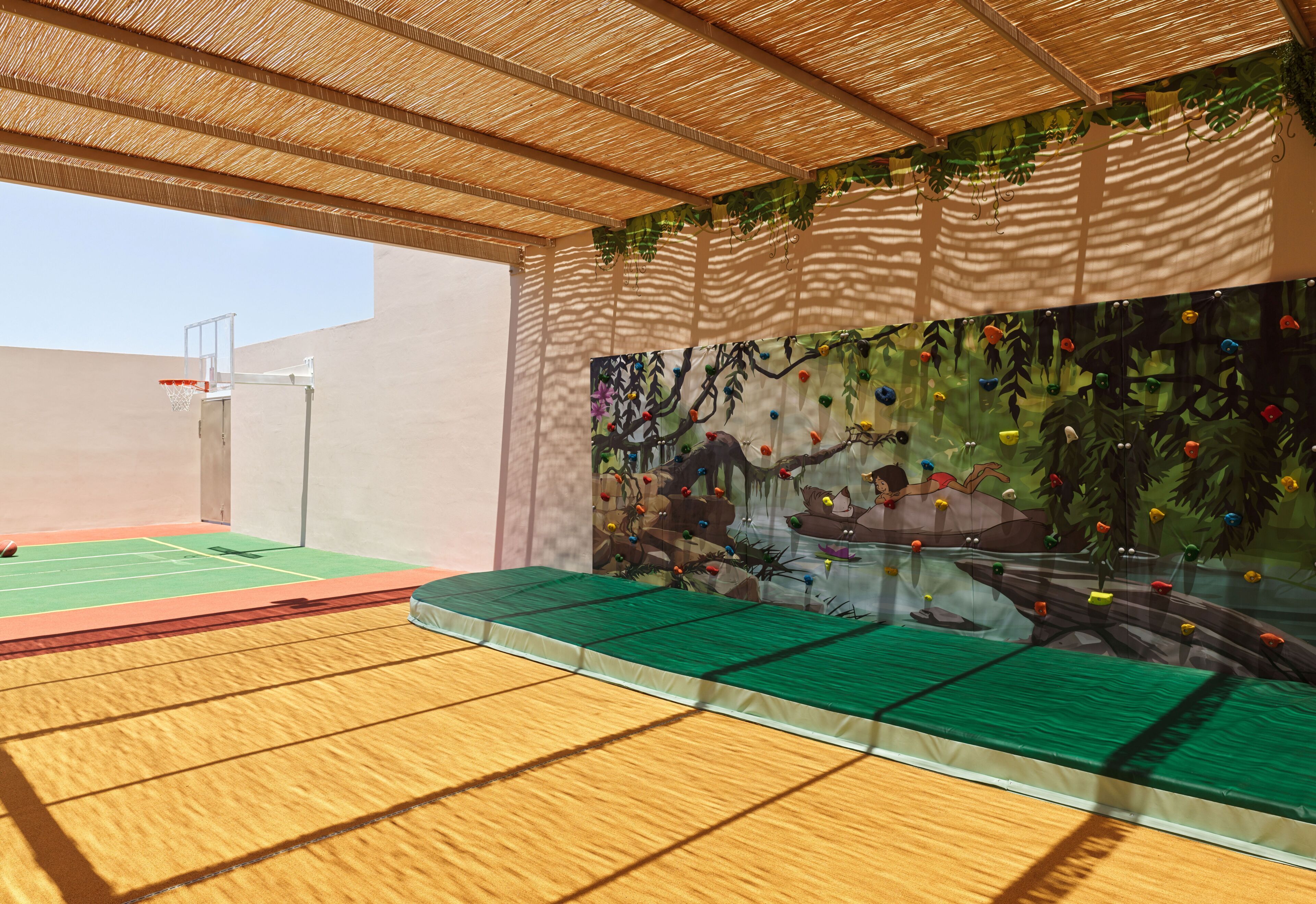 An indoor sports area with a basketball court, climbing wall, and a green cushioned seating area.
