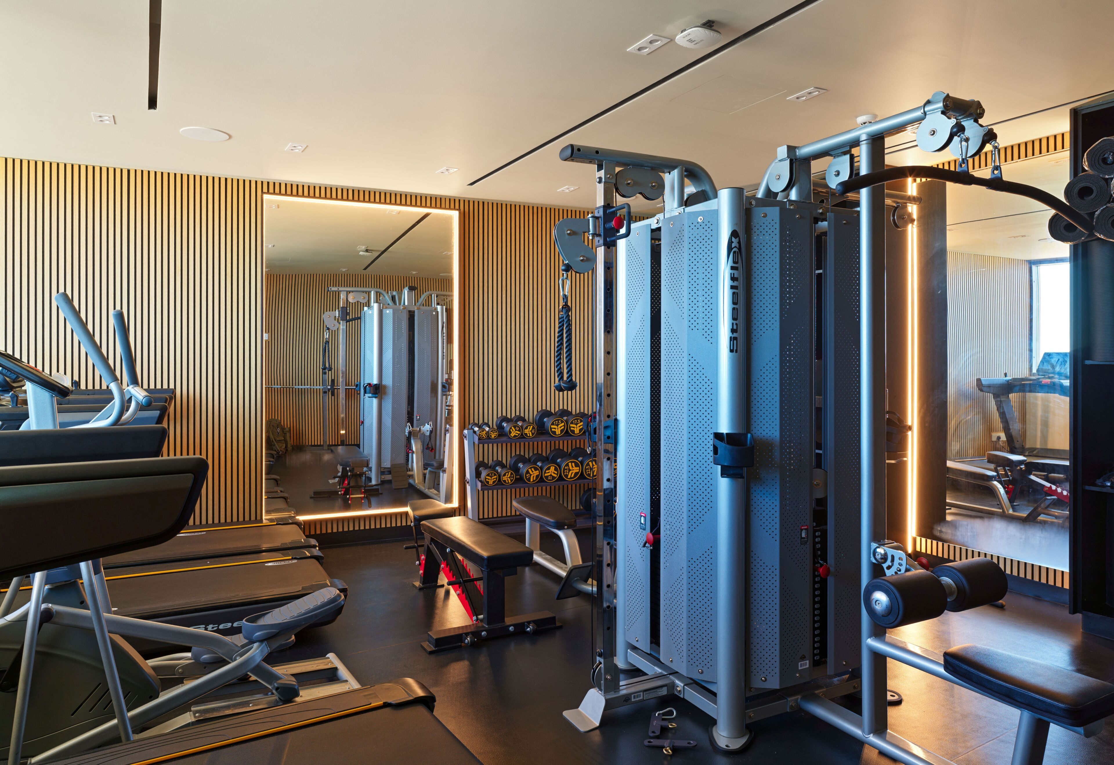Une salle de sport moderne équipée de matériel d’exercice, d’un tapis de course et d’un mur recouvert de miroirs.