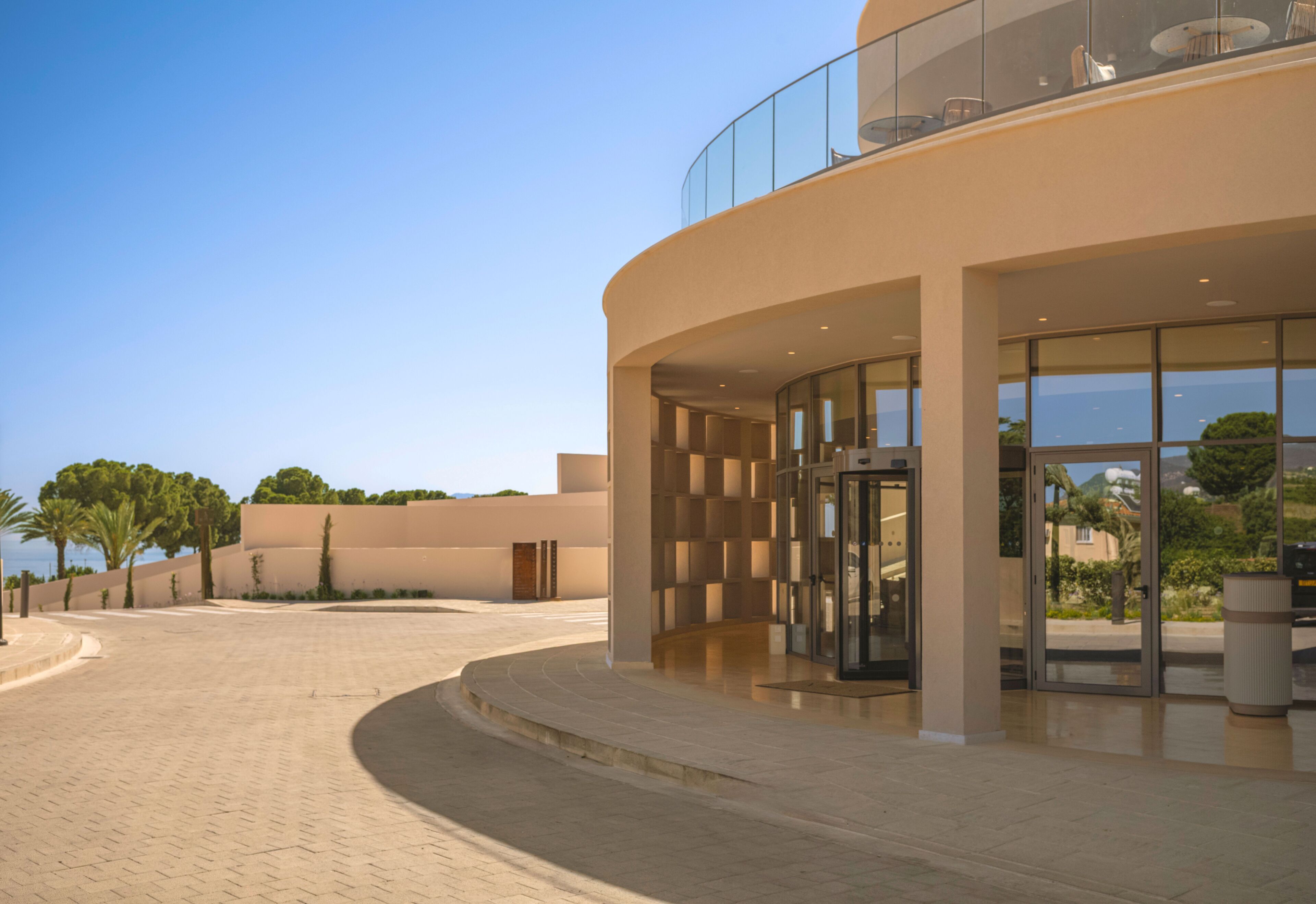A modern building with a curved facade, large glass entrance, and a balcony overlooking the entrance.