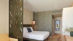 A modern hotel room with a bed, a sofa, a dining table, and a decorative wall panel. - NALU Latchi Leonardo Limited Edition (Polis)