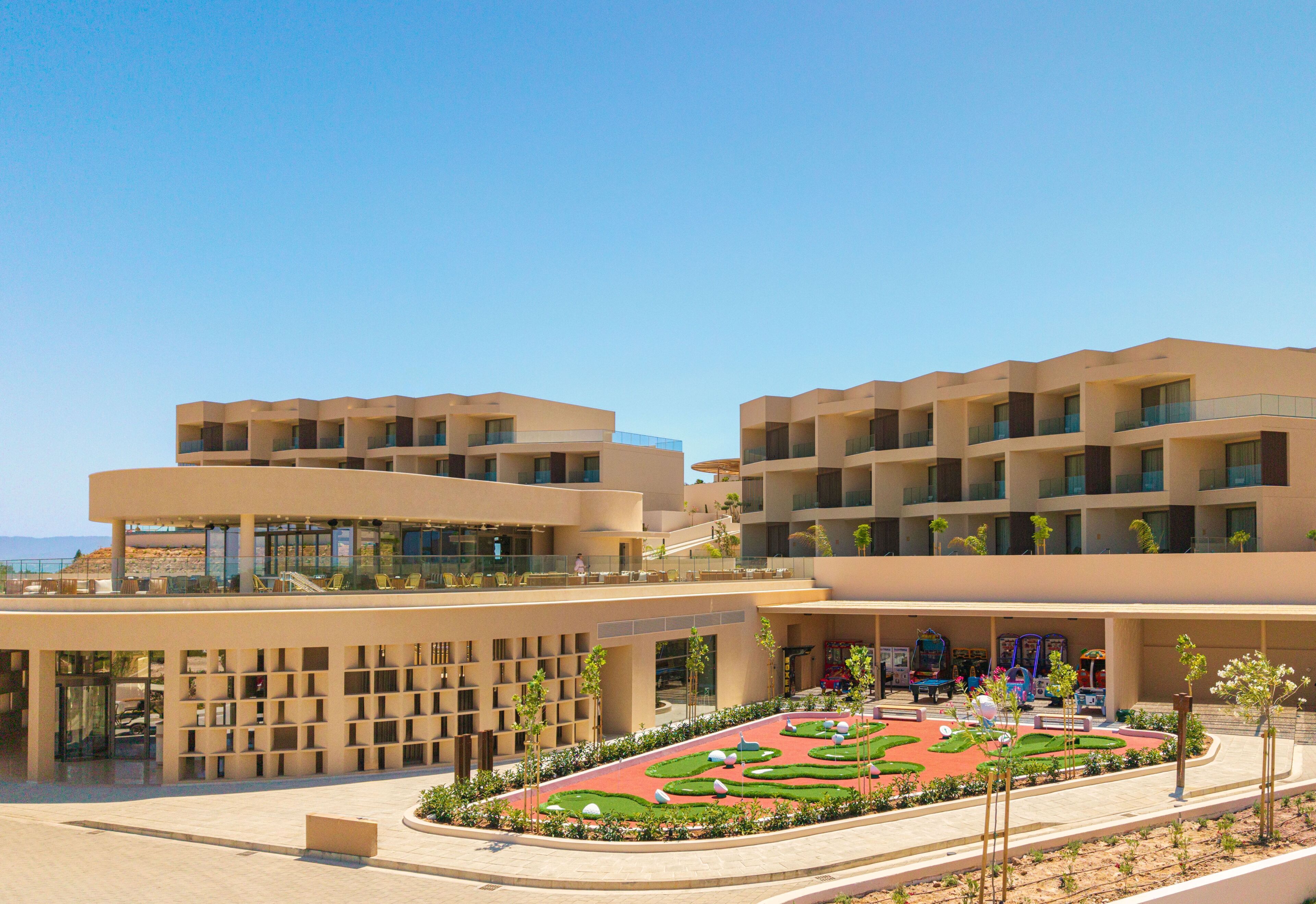 Un hotel moderno con varias plantas, asientos exteriores y un jardín ajardinado.